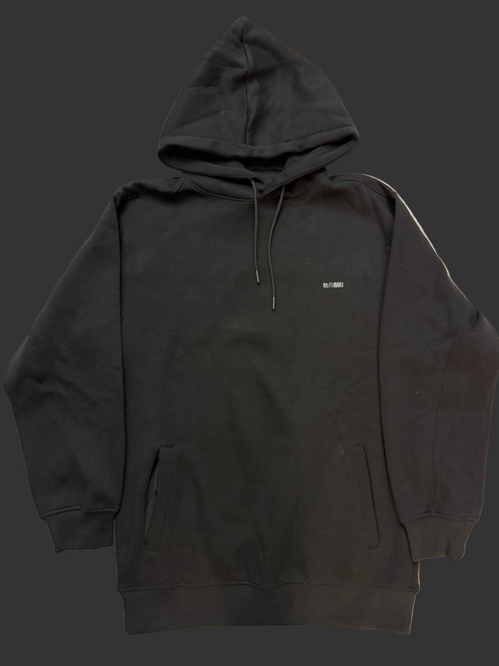 A black pullover hoodie laid flat on a light-colored fabric surface, featuring a kangaroo pocket, drawstrings, and a small white text logo on the chest.