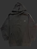 A black pullover hoodie laid flat on a light-colored fabric surface, featuring a kangaroo pocket, drawstrings, and a small white text logo on the chest.