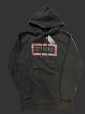 A black pullover hoodie with a graphic chest print reading 'REMAKE' inside a dusty pink rectangular border, laid flat on a light beige fabric background. A hangtag is attached near the collar.
