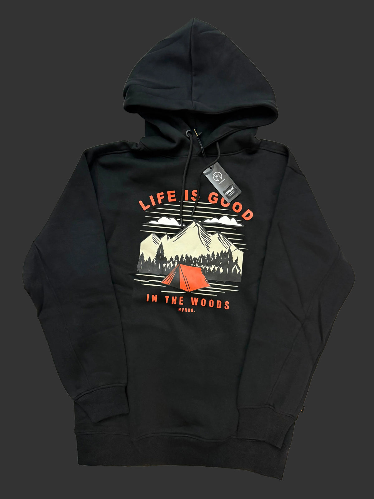 A black pullover hoodie laid flat on a light fabric background, featuring a front graphic with the text 'LIFE IS GOOD' and 'IN THE WOODS' around an illustrated mountain scene with a red tent.