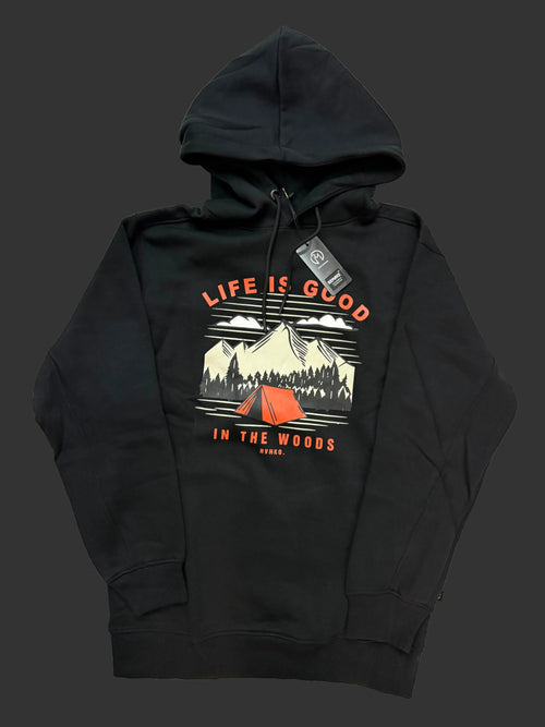 A black pullover hoodie laid flat on a light fabric background, featuring a front graphic with the text 'LIFE IS GOOD' and 'IN THE WOODS' around an illustrated mountain scene with a red tent.