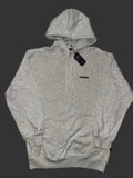 A oatmeal gray pullover hoodie with a half-zip neckline, featuring a small red 'REMAKE' logo on the left chest and a black hangtag, laid flat on a light gray patterned fabric background.